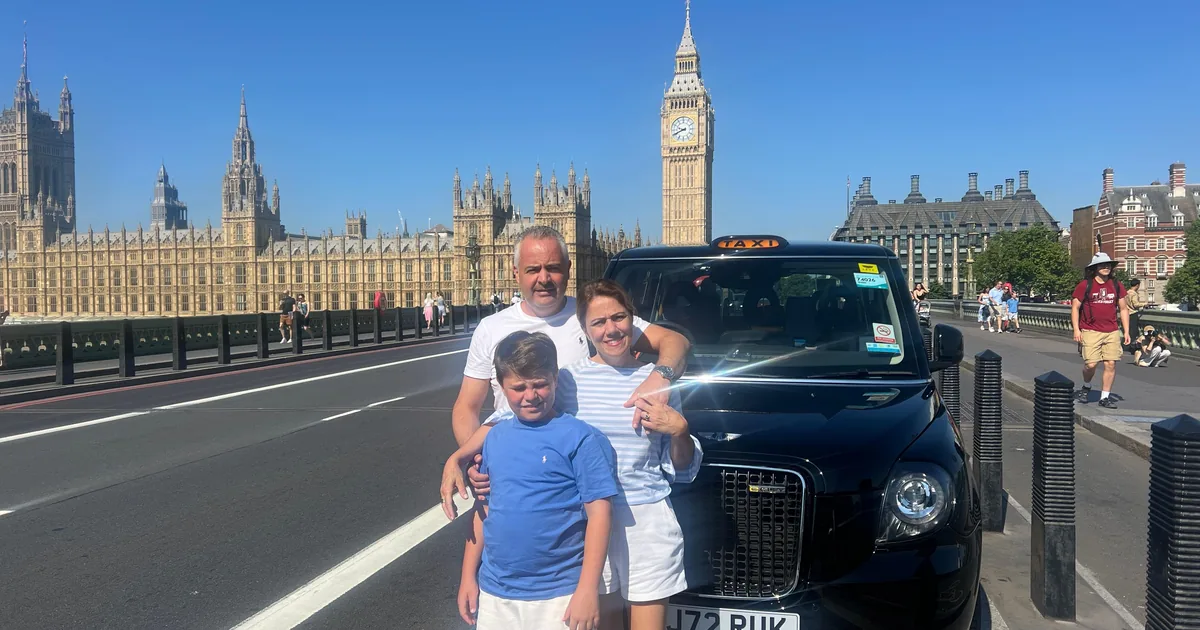 A family beside a black cab on Westminster Bridge, the Houses of Parliament and Big Ben behind
