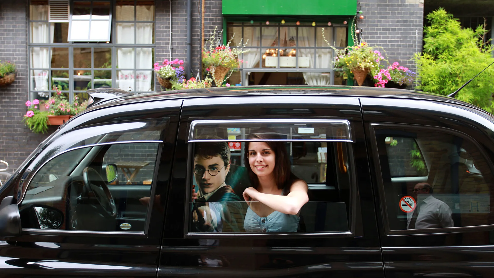A guest at the window of a black cab beside a Harry Potter cut-out, from the Harry Potter film locations tour listing