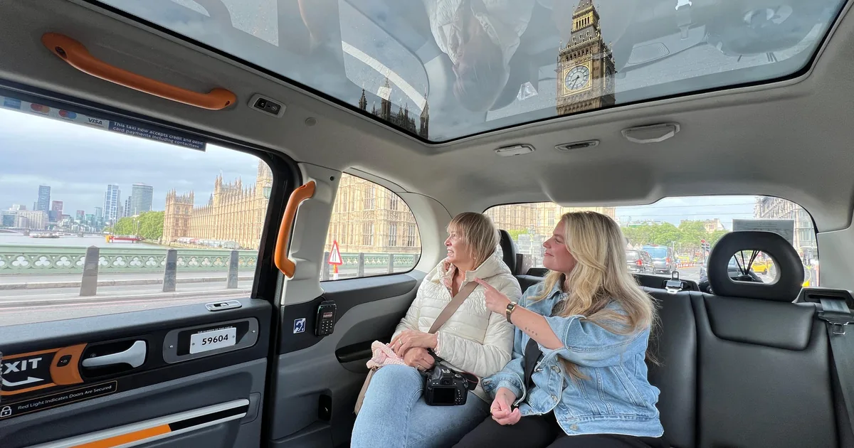 Two guests on the rear seat of an electric London taxi, Big Ben seen through the panoramic glass roof